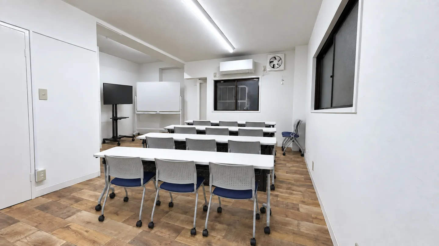 スクール形式で机と椅子を並べた会議室のイメージ。65インチモニターとホワイトボードが奥に見える